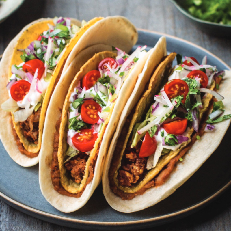 A picture of three tacos in a round gray tray.