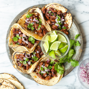 Five mexican tacos in a round plate with a bowl of lime.