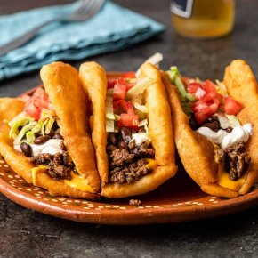 Three navajo tacos in a round brown plate on a table.