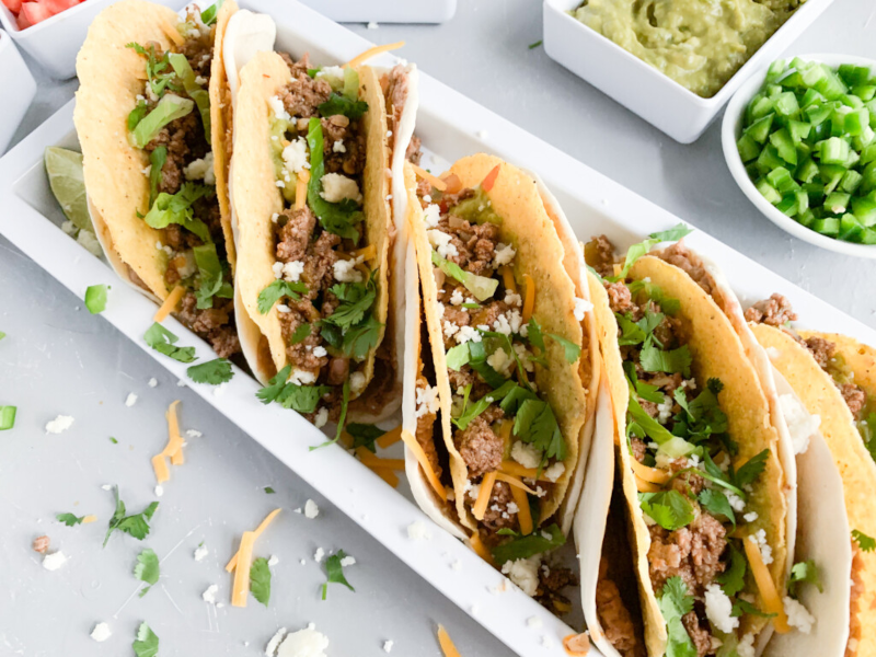 Five double decker tacos in a white serving plate on a table.