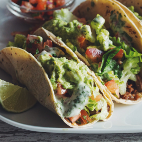 Two vegan tacos on a plate with a bowl of toppins.