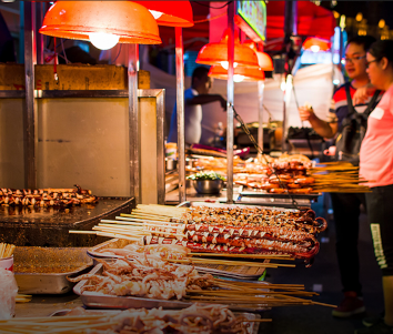 Two girls browsing skewers at a street food stall